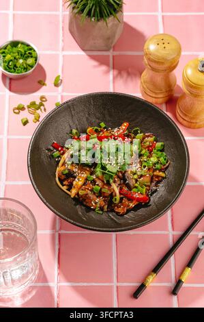 Schüssel mit asiatischen Nudeln mit Rindfleisch und Gemüse auf rosa Fliesen Stockfoto
