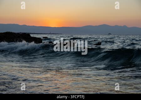 Ozeanwellen rollen an einer felsigen Küste bei Sonnenuntergang Stockfoto