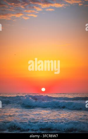 Vertikale Aufnahme eines lebhaft roten Sonnenaufgangs über schäumenden Meereswellen Stockfoto