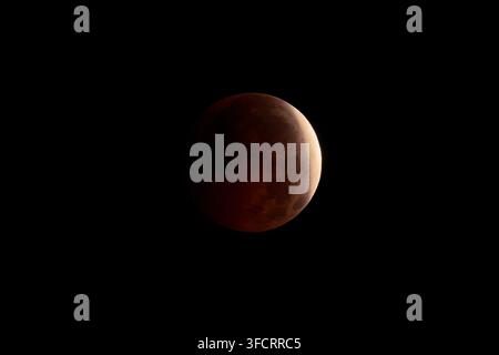 Blutmond leuchtet tiefrot und teilweise im Schatten während einer totalen Mondfinsternis, dramatisches Himmelspektakel vor dem weiten dunklen Nachthimmel und fernen Sternen Stockfoto