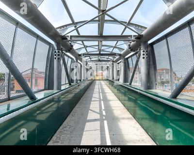 Perspektivansicht in einer modernen überdachten Fußgängerbrücke mit Stahlkonstruktion, grünen Schutzpaneelen, Drahtgitter-Sicherheitswänden und transparenter Stockfoto