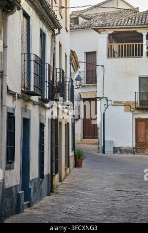 Ruhige enge Straße im historischen Baeza mit weiß getünchten Fassaden, schmiedeeisernen Balkonen, Holztüren und traditionellen Ziegeldächern. Stockfoto