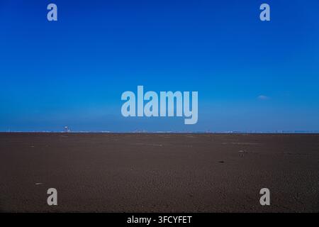 Weite leere Schlickfläche unter einem klaren tiefblauen Himmel mit entfernter Horizontlinie, Breitbild-Aufnahme in niedriger Perspektive. Stockfoto