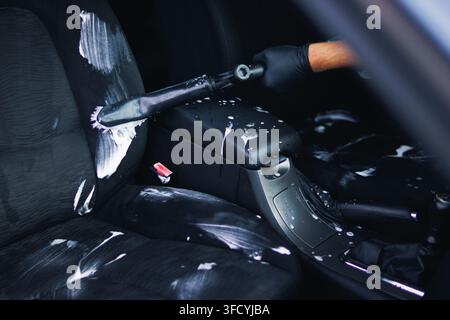 Professioneller Autolackier-Service reinigt das Fahrzeuginnere, trägt Schaumshampoo auf die Polster auf, pflegt die Autositze und führt eine gründliche Tiefenreinigung durch Stockfoto