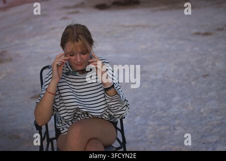 Junge Frau sitzt im Freien in einem gestreiften Hemd, hält Sonnenfinsternisbrillen, vertieft in wissenschaftliche Beobachtung während eines Himmelsereignisses, demonstriert Stockfoto