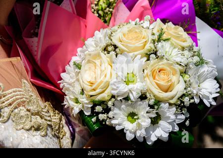 Atemberaubender Nahaufnahme eines farbenfrohen Hochzeitsstraußes mit cremeweißen Rosen, frischen Chrysanthemen und zarten Schleierblumen, umhüllt in Pi Stockfoto