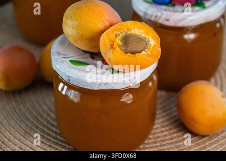 Frische ganze und gehaltene Aprikosen ruhen auf dem Deckel eines Glases, das mit hausgemachter Aprikosenmarmelade gefüllt ist. Stockfoto