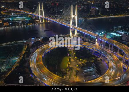 Luftaufnahme der Nanpu-Brücke bei Nacht mit beleuchteter kreisförmiger Rampe und Lichtspuren vom Verkehr in Shanghai, Shanghai, China. Stockfoto