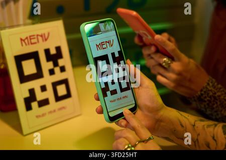Junge Frauen scannen QR-Code-Menü mit Smartphones in einem asiatisch stilisierten Café Stockfoto