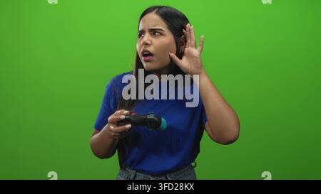 Frau, die mit der rechten Hand Gamepad hält, während sie im Studio von der linken Hand an das Ohr schwingt, zuhört und zuhört, als würde sie Audiosignale hören; Verwirrtheit Neugier. Stockfoto