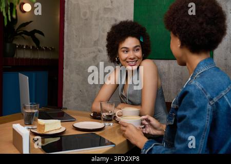 Zwei schöne junge afroamerikanische Frauen genießen warme Getränke und Lachen zusammen. Stockfoto