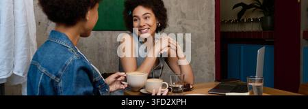 Zwei wunderschöne junge afroamerikanische Frauen genießen ein herzliches Gespräch, während sie Kaffee schlürfen. Stockfoto