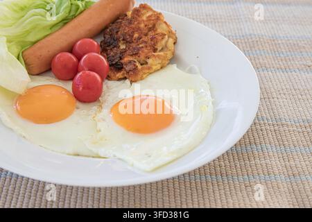 Gebratene Eier mit Wursttomaten, Salat und angebratenem Patty auf dem Teller Stockfoto
