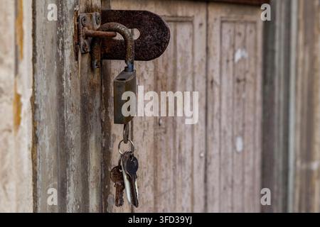 Ein rostiges Vorhängeschloss und alte Schlüssel hängen an einem verwitterten Riegel an einer abblätternden Holztür, Valletta, Malta Stockfoto