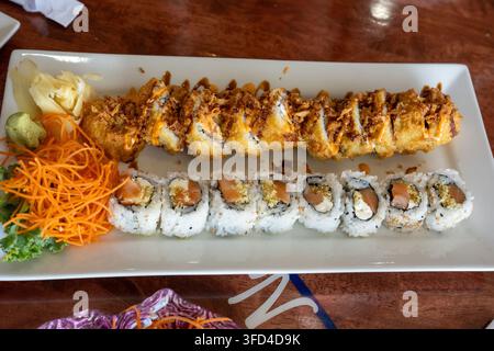 Nahaufnahme von verschiedenen Sushi-Rollen, die auf einem weißen rechteckigen Teller in einem japanischen Restaurant serviert werden. Das Tablett enthält Lachsrollen, knusprig gebratenes Sushi w Stockfoto