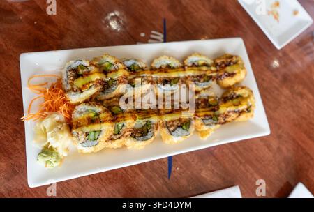 Oberblick über verschiedene knusprige Sushi-Rollen, die auf einem weißen rechteckigen Teller mit Soße, geriebener Karotte, Ingwer und Wasabi angeordnet sind. Japanisches Restaurant Stockfoto