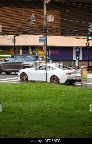 Weißer Ford Mustang GT fährt auf einer städtischen Stadtstraße, Seitenrückansicht Stockfoto