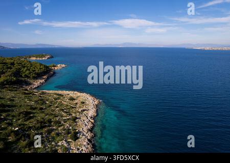 Drohnenaufnahme der wilden, felsigen Insel Moni, umgeben vom tiefblauen Ägäischen Meer. Steile Klippen, grüne Kiefern und Hügel unter einem klaren blauen Himmel. Stockfoto
