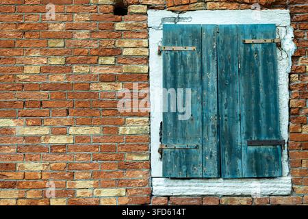 Vintage-blaue Holzfensterläden an einer alten roten Backsteinmauer. Stockfoto