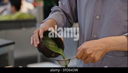 Barista gießt Matcha-Tee durch einen Metallfilter aus einer Keramikschüssel. Professionelle Zubereitung von japanischem Grüntee in einer Café-Umgebung. Stockfoto