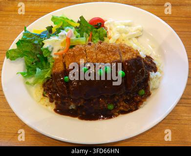 Ein Teller mit lokaler Gourmet-Schnitzel, einem panierten Schweineschnitzel mit dunkler Demiglace-Sauce und grünen Erbsen, serviert über Butterreis mit einer Beilage Stockfoto