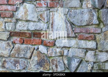 Verwitterte Steinmauer mit unregelmäßiger Mauerarbeit und freiliegendem rotem Ziegel Stockfoto