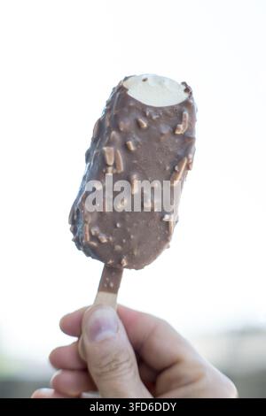 Eine Person hält eine mit Schokolade überzogene Eisstange an einem Stock. Stockfoto