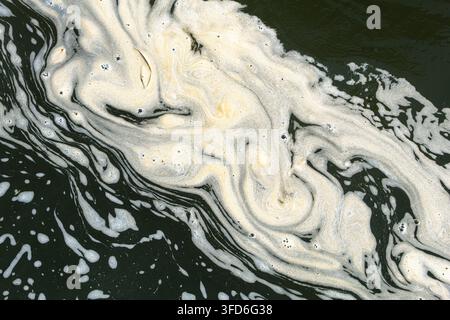 Abstrakter Nahaufnahme von cremiger weißer Schaum, der sich über dunkles grünes Wasser schlängelt und flüssige marmorierte Muster und natürliche Texturen erzeugt. Stockfoto