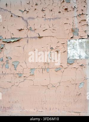 Verwitterte hellbraun gestrichene Betonwand in Nahaufnahme mit vertikalen Rissen, abblätternder Farbe, freiliegendem Zement und einem abgeplatzten weiß gestrichenen Rechteck Stockfoto