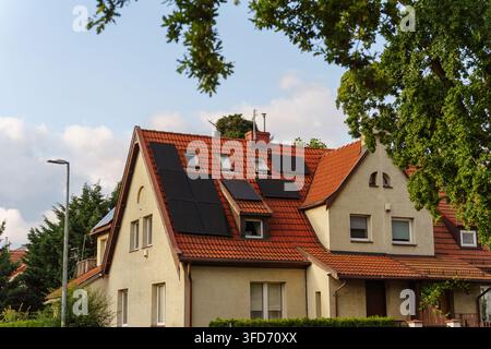 Wohnhaus mit solaren Photovoltaik-Paneelen, die auf einem roten Ziegeldach installiert sind, das moderne nachhaltige erneuerbare Energielösungen präsentiert Stockfoto