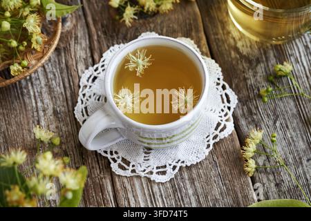 Lindenblütentee in einer weißen Keramiktasse auf einem Holztisch, Nahaufnahme Stockfoto