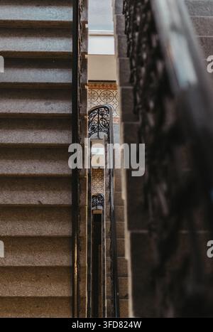 Ein Blick eine kunstvolle Steintreppe hinunter zeigt dekorative schmiedeeiserne Geländer und gemusterte Fliesenbeläge auf den Podesten unten. Stockfoto