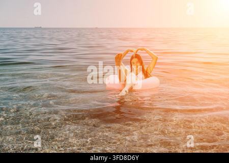 Frau im Bikini beim Wassertubing, macht mit Füßen und Händen ein Herzzeichen während eines Sommerurlaubs in klarem Ozean mit Kopierraum. Stockfoto