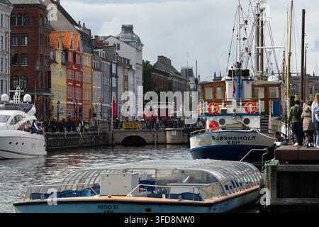 Touristen erkunden den ikonischen Nyhavn-Kanal in Kopenhagen, Dänemark, und bewundern die historischen farbenfrohen Gebäude und die dort liegenden Ausflugsboote. Stockfoto