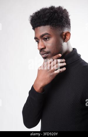 Ein junger Mann mit dunkler Haut und einer Afro-Frisur schaut nachdenklich nach unten, während er sein Kinn auf die Hand stützt Stockfoto