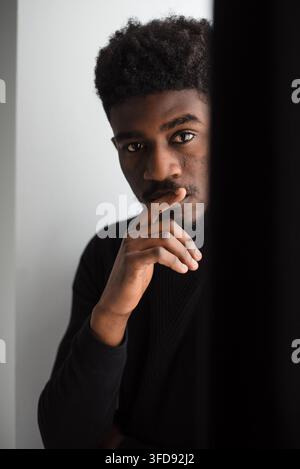 Ein nachdenklicher junger Mann mit dunkler Haut und einer Afro-Frisur blickt den Betrachter direkt an, während er sein Kinn auf die Hand stützt Stockfoto