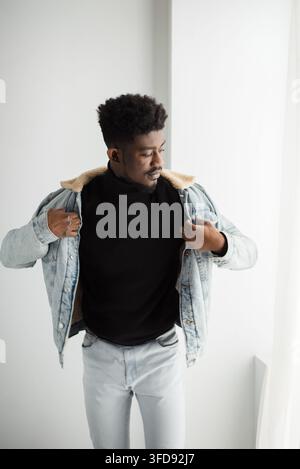 Ein stilvoller junger Mann mit Afro-Frisur posiert selbstbewusst in einem Studio und präsentiert sein modisches Outfit, während er von der Kamera wegschaut Stockfoto