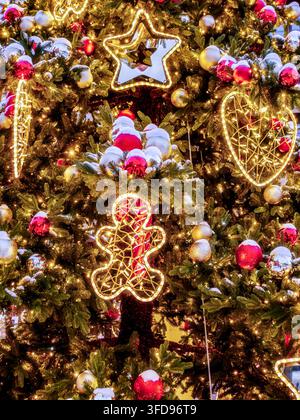 Eine Nahaufnahme eines festlichen Weihnachtsbaums, der mit warmem Licht, roten und goldenen Ornamenten, schneebedeckten Zweigen und beleuchteten Dekorationen glüht, die eine gemütliche Atmosphäre vermitteln Stockfoto