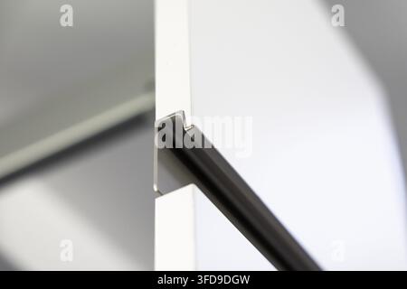 Eine nahaufnahmeabstrakte Ansicht einer modernen Schranktür mit einem dunklen, integrierten Griff und sauberen weißen Oberflächen Stockfoto