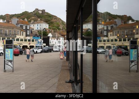 Zwei Personen gehen durch das historische Stade-Gebiet von Hastings, überragt von der Wahrzeichen-East-Hill-Lift oben auf der Klippe in East Sussex. Stockfoto