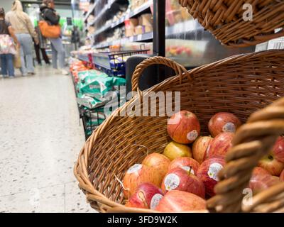 Nahaufnahme von roten und grünen Äpfeln, die in einem Weidenpräsentkorb in der Obstabteilung eines Supermarkts gestapelt sind. Einkäufer weiter unten im Gang im weichen Fokus UK Stockfoto