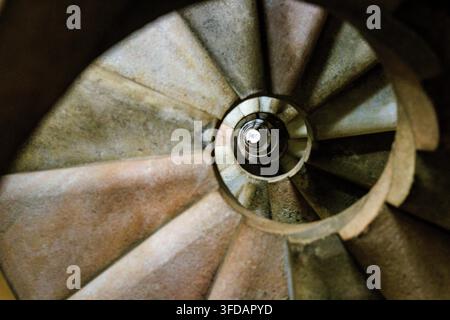 Abstrakte Ansicht von oben einer steinernen Wendeltreppe, bei der sich die Stufen eng zu einem hellen kreisförmigen Zentrum winden, das einen hypnotischen Tunneleffekt erzeugt. Stockfoto