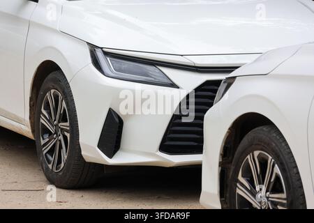 Eine weiße Fahrzeugfront, die im Freien geparkt ist, mit beschädigtem Stoßstangen und einem nah geparkten Auto, das eine dramatische Autoszene erzeugt Stockfoto