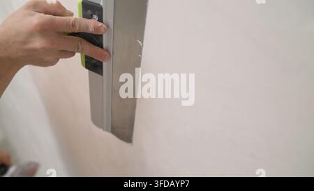 Mann richtet die Wände aus. Nahaufnahme von menschlichen Händen, die an einer Betonwandstruktur arbeiten. Spachtel in der Hand, Nahaufnahme. Stockfoto
