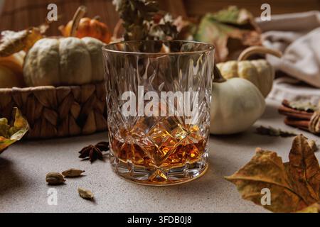 Kristallglas gefüllt mit Whisky, das in der Nähe von weißen Kürbissen, Kardamomkapseln und Zimtstangen platziert ist.. Stockfoto