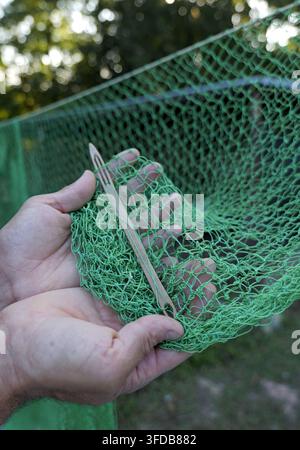 Hände weben ein grünes Fischernetz mit einem Holzschiff, Nahaufnahme zeigt traditionelle Knottechnik, geschicktes Handwerk und geduldiger outdoor Mannua Stockfoto