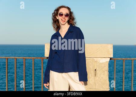Kandidates Portrait einer kaukasischen Frau mit lockigem Haar, die eine Sonnenbrille trägt und eine lustige Grimasse macht, während sie in die Kamera schaut Stockfoto