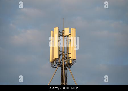 Eine Dach-Funkzellenturmantenne steht auf einem modernen Gebäude vor einem bewölkten blauen Himmel bei Sonnenuntergang montiert. Stockfoto