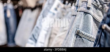 Reihen von hellen und dunkelblauen Denimhosen, die an einer Kleiderstange in einem modernen Bekleidungsgeschäft hängen Stockfoto