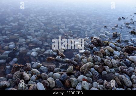 Eine ruhige Szene mit komplexen Texturen auf abgenutzten Steinen in einer teilweise untergetauchten Wasserumgebung bei bewölkten Bedingungen. Stockfoto
